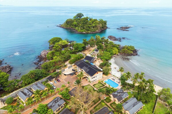 An aerial view of a coastal property with a beach, a small island, and a swimming pool.