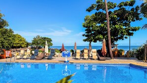 A pool with lounge chairs and umbrellas, a sign with a logo, and a view of the ocean. - Mozza Beach Resort (York)