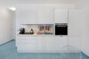 A modern kitchen with white cabinets, a gas stove, a kettle, a sink, and a refrigerator.
