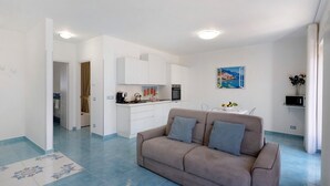 A modern living room with a sofa, a kitchen area with white cabinets, and a dining table. - Apartment 'La Dimora Dei Nonni' with Mountain View, Wi-Fi and Air Conditioning (Agerola)