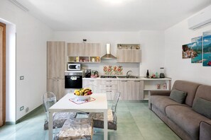 A modern kitchen with light wood cabinets, a dining table with chairs, a sofa, and a kitchen island with a sink and stove. - Apartment 'La Dimora Dei Nonni' with Mountain View, Wi-Fi and Air Conditioning (Agerola)