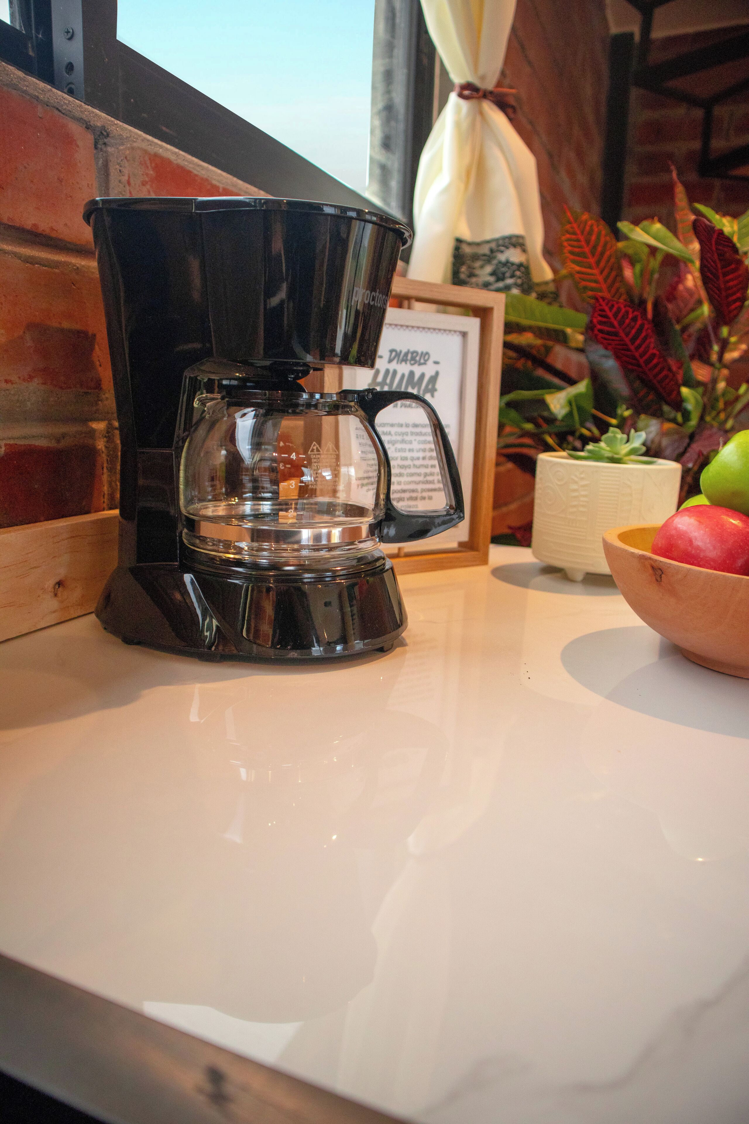 Une machine à café posée sur un plan de travail, avec un cadre contenant une photo et un bol de fruits.