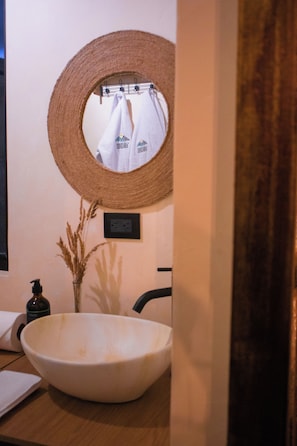 Ein Badezimmer mit einem großen weißen Waschbecken, einem gewobenen Spiegel und einem Handtuchhalter mit einem weißen Handtuch.