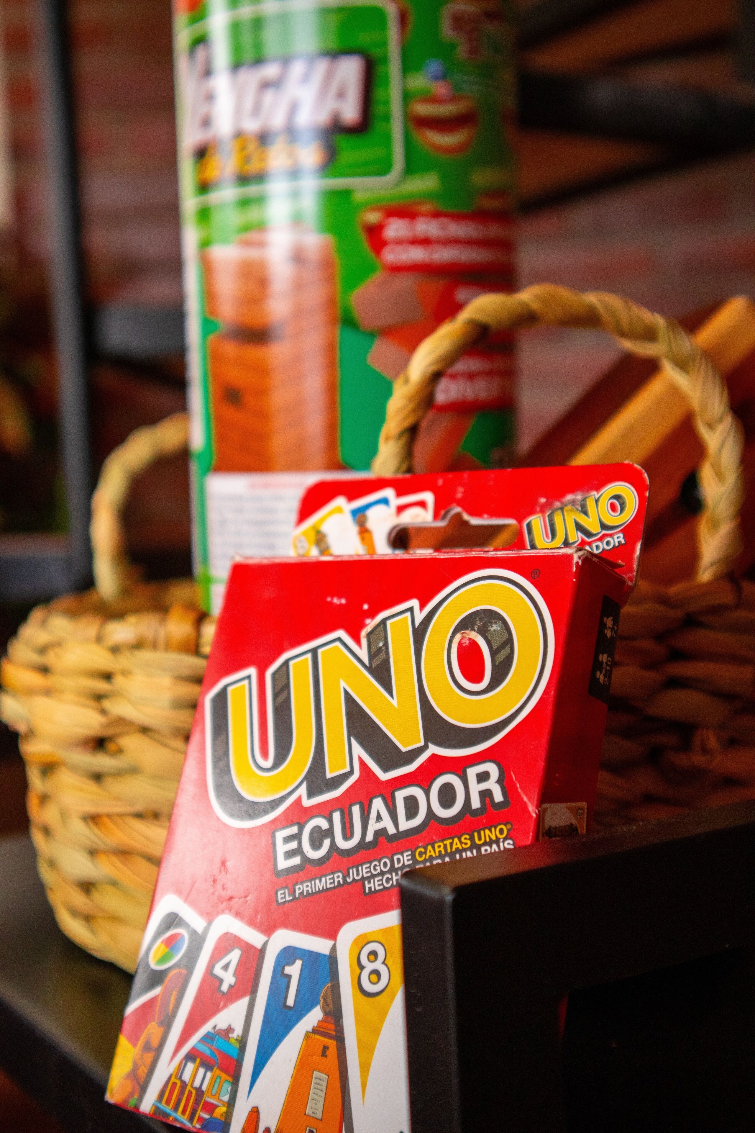 A Uno Ecuador card game box on a table with a woven basket and a can of beverage in the background.