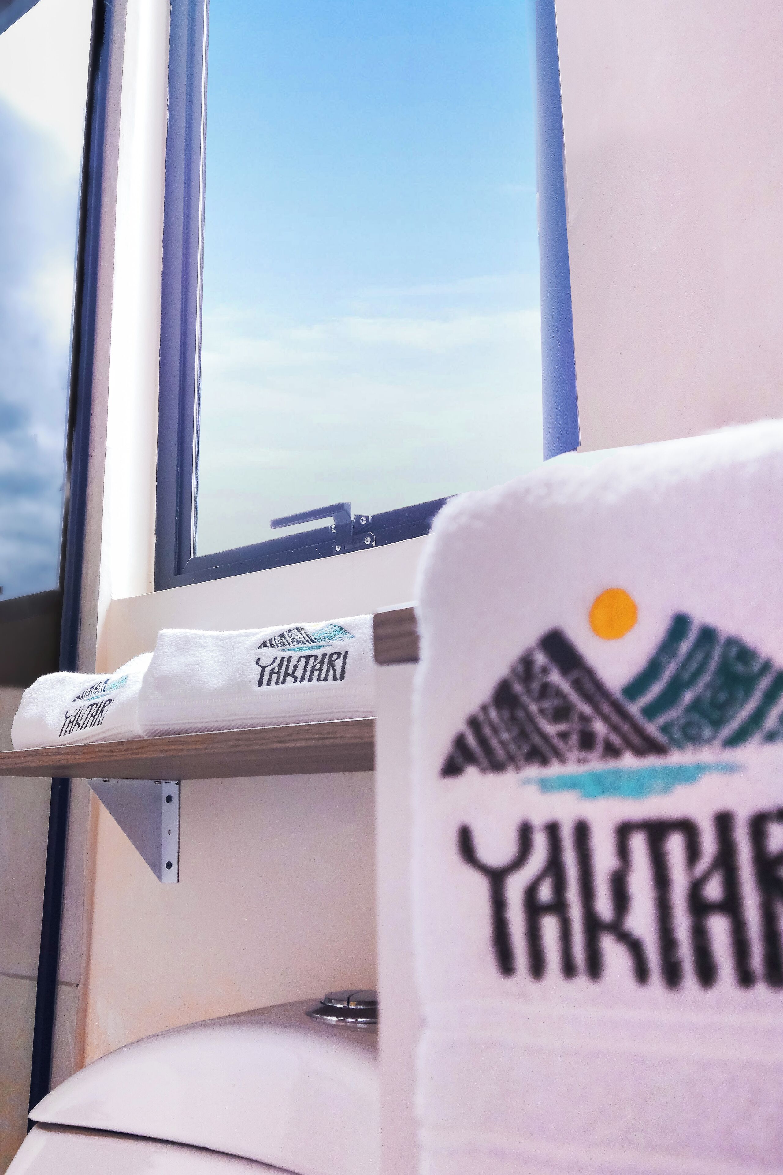 Et vindue med udsigt til himlen og et håndklæde med teksten 'YAKTHARI'.