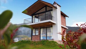 Una casa moderna a due piani con un balcone, ampie finestre e vista sul paesaggio circostante.