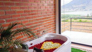Un bagno con una vasca da bagno piena di petali di rosa, una pianta in vaso e vista su un paesaggio montuoso.