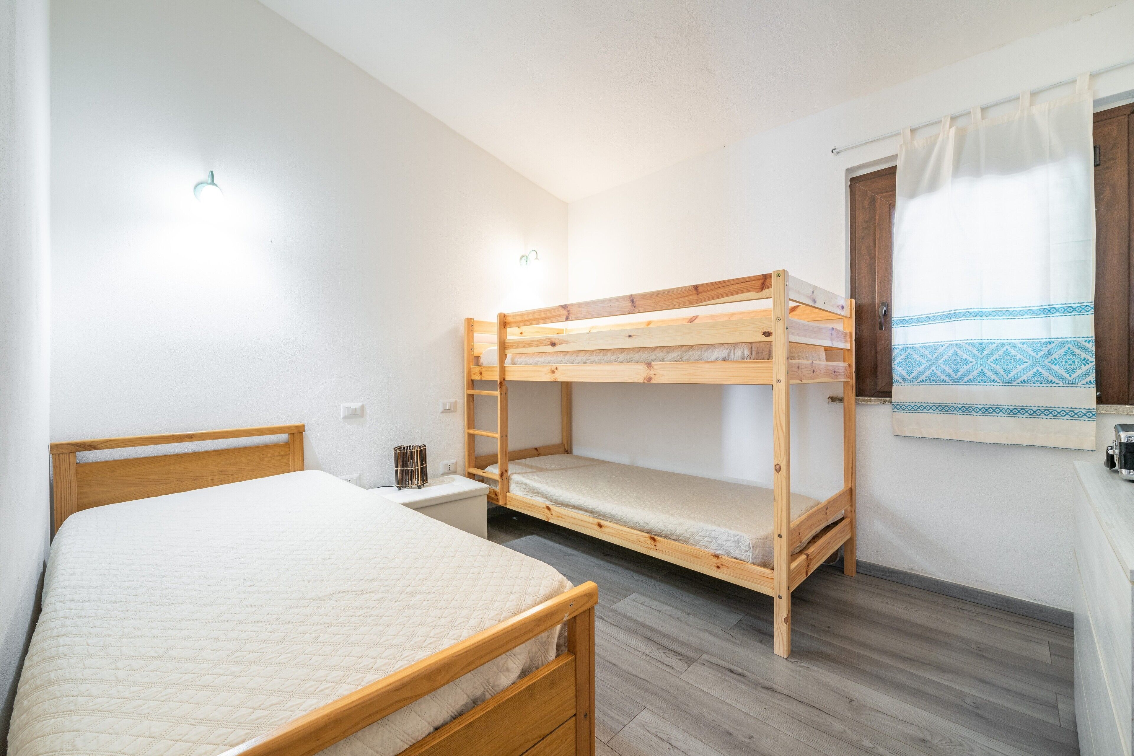 A room with a single bed, a bunk bed, a small table, and a window with curtains.
