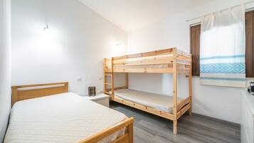 A room with a single bed, a bunk bed, a small table, and a window with curtains.