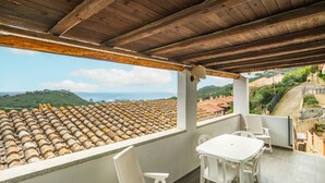 Un balcón con vistas a tejados de teja, sillas blancas y una mesa.