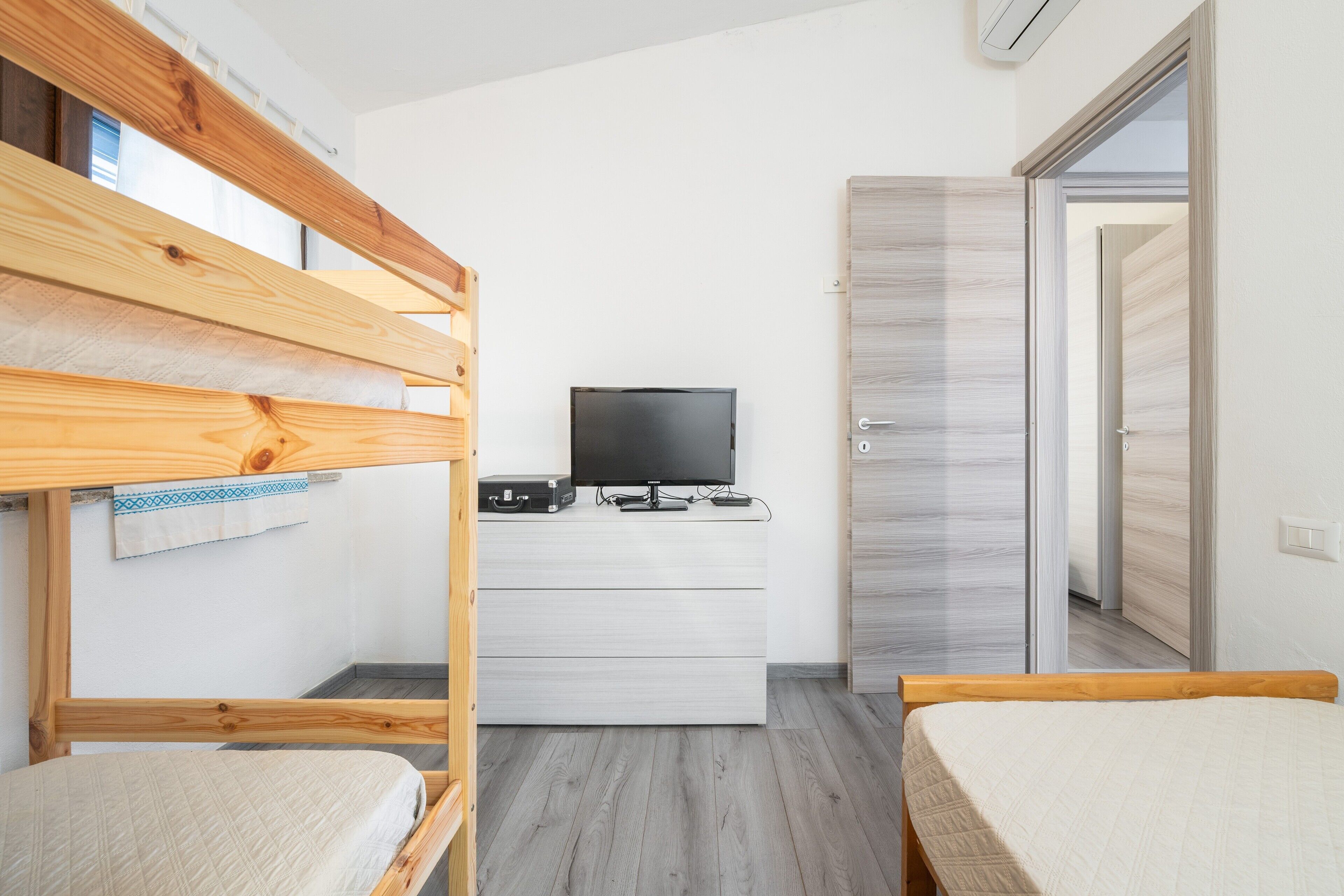 A room with bunk beds, a flat-screen TV, a wooden desk, and a wardrobe.