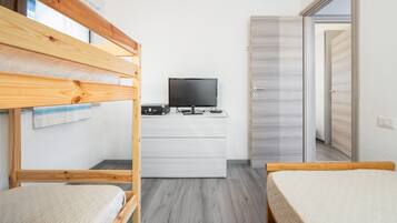A room with bunk beds, a flat-screen TV, a wooden desk, and a wardrobe.