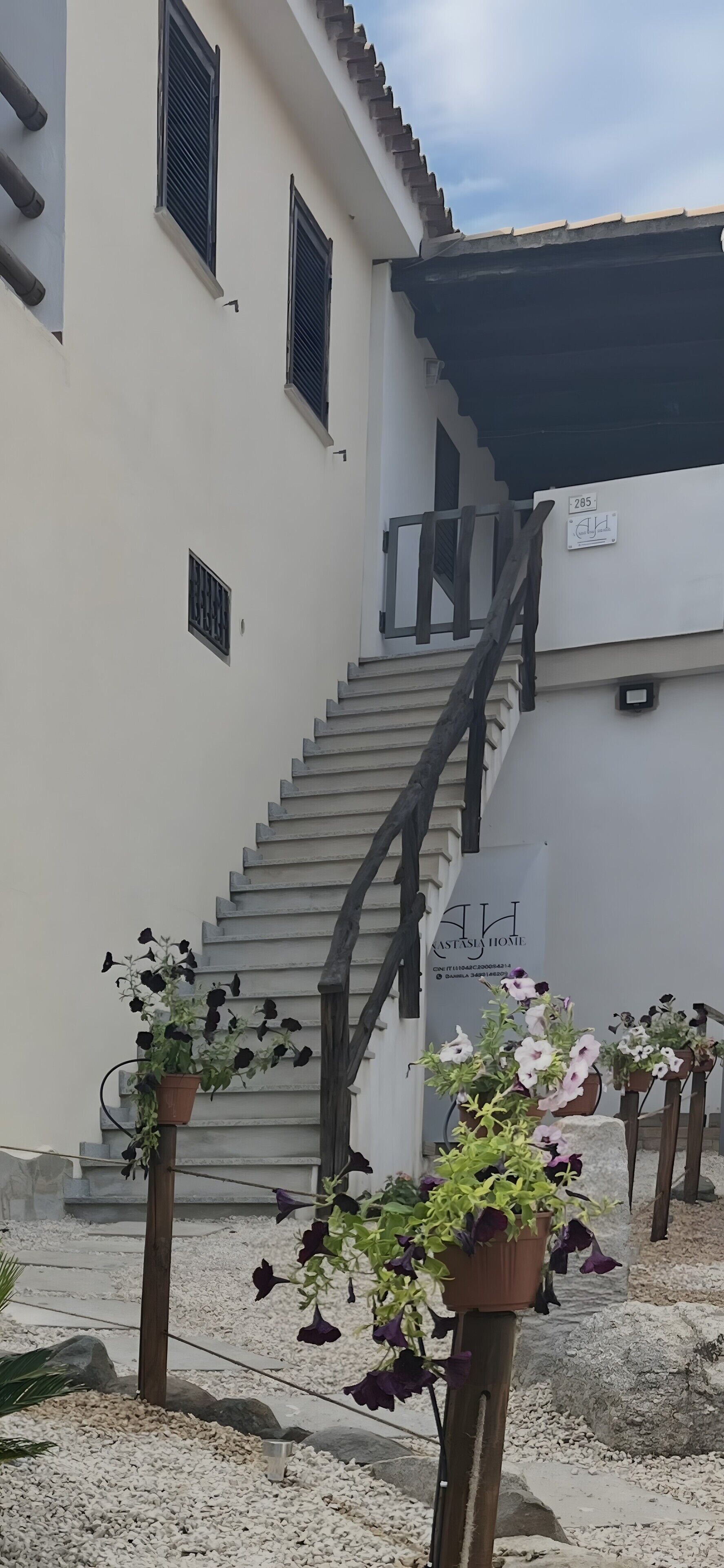 En trappe fører op til en bygning, hvor der på væggen står et skilt med 'ASTALIS HOME' og nummeret '285'.