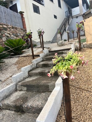 Una escalera de piedra que conduce a un edificio de fachada blanca, rodeado de grava y plantas en macetas.