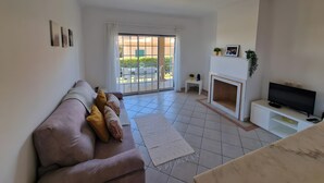 Ein Wohnzimmer mit einer Couch, einem Fernseher, einem Kamin und einer Glastür zu einer Terrasse.