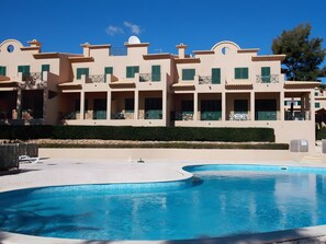 Un hôtel doté de nombreux balcons, d’une piscine et d’une haie bien entretenue.