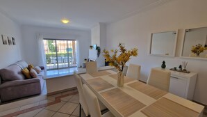 Ein modernes Wohnzimmer mit einer Couch, einem Esstisch, Stühlen und Blick durch eine Glastür auf einen Außenbereich.