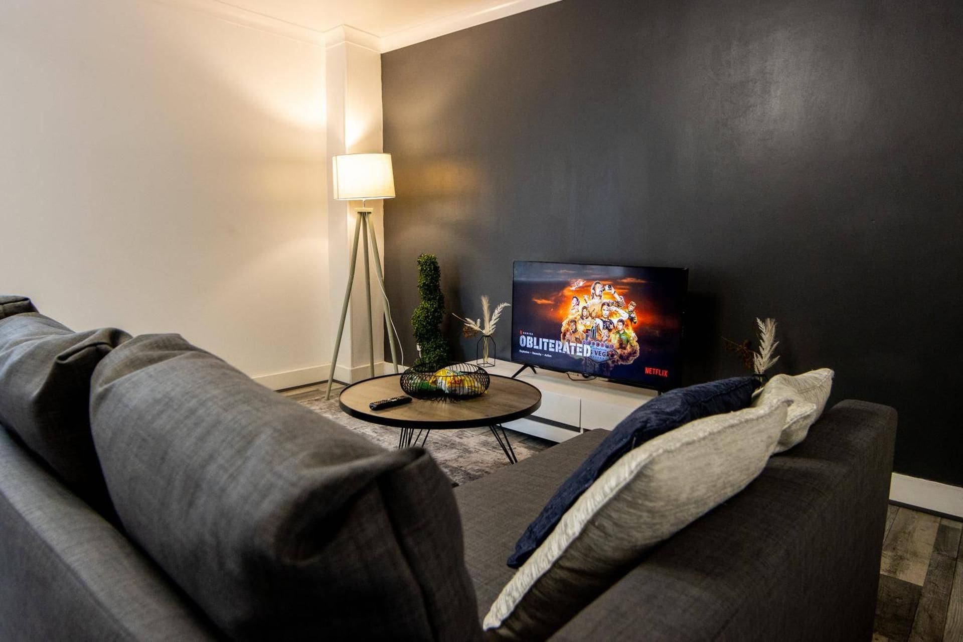 Una sala de estar con una pared oscura, una mesa de centro redonda, un sofá y un televisor mostrando un cartel de película.
