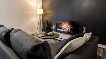 Una sala de estar con una pared oscura, una mesa de centro redonda, un sofá y un televisor mostrando un cartel de película.