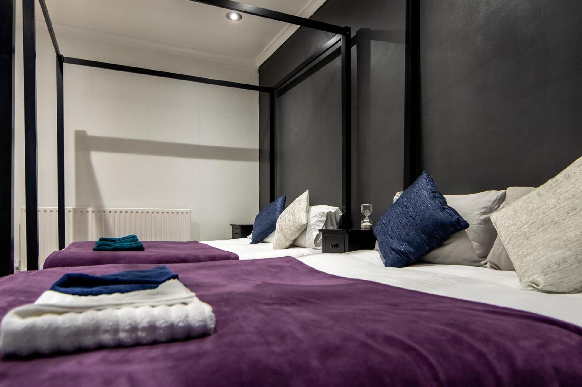 A modern hotel room with two beds, each with a purple bedspread and multiple pillows.
