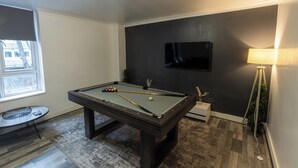 Une table de billard avec des billes, un téléviseur fixé au mur et une lampe.
