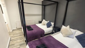 Une chambre avec un lit à baldaquin, dotée de deux lits, chacun recouvert d’une courtepointe et agrémenté d’oreillers violets, et un radiateur blanc en arrière-plan.