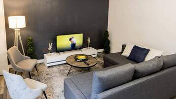 A modern living room with a grey sofa, a white armchair, a round coffee table, and a flat-screen TV on a white stand.