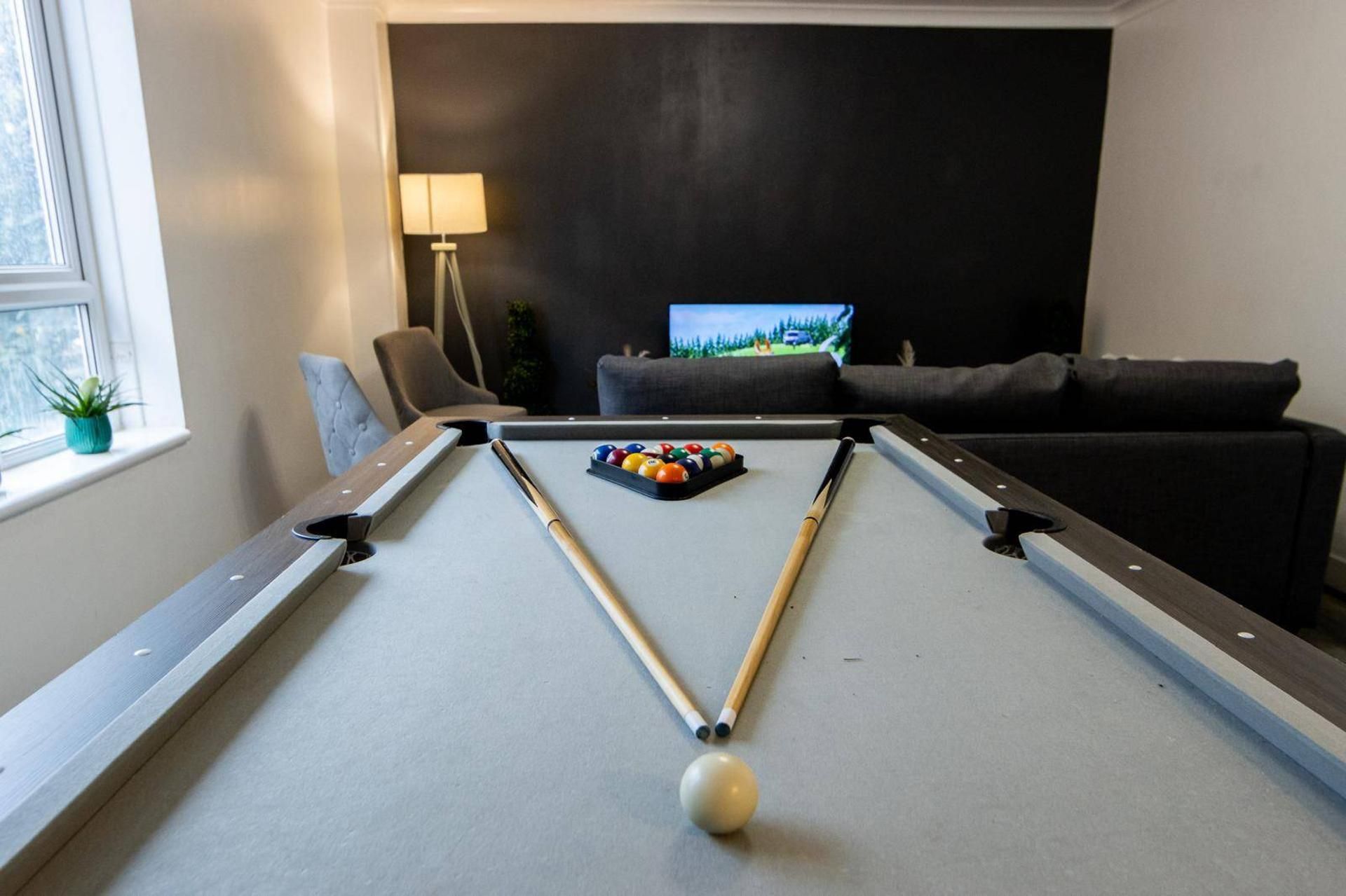 A pool table with a cue ball and billiard balls, a television in the background, and a sofa.