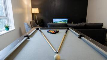 A pool table with a cue ball and billiard balls, a television in the background, and a sofa.