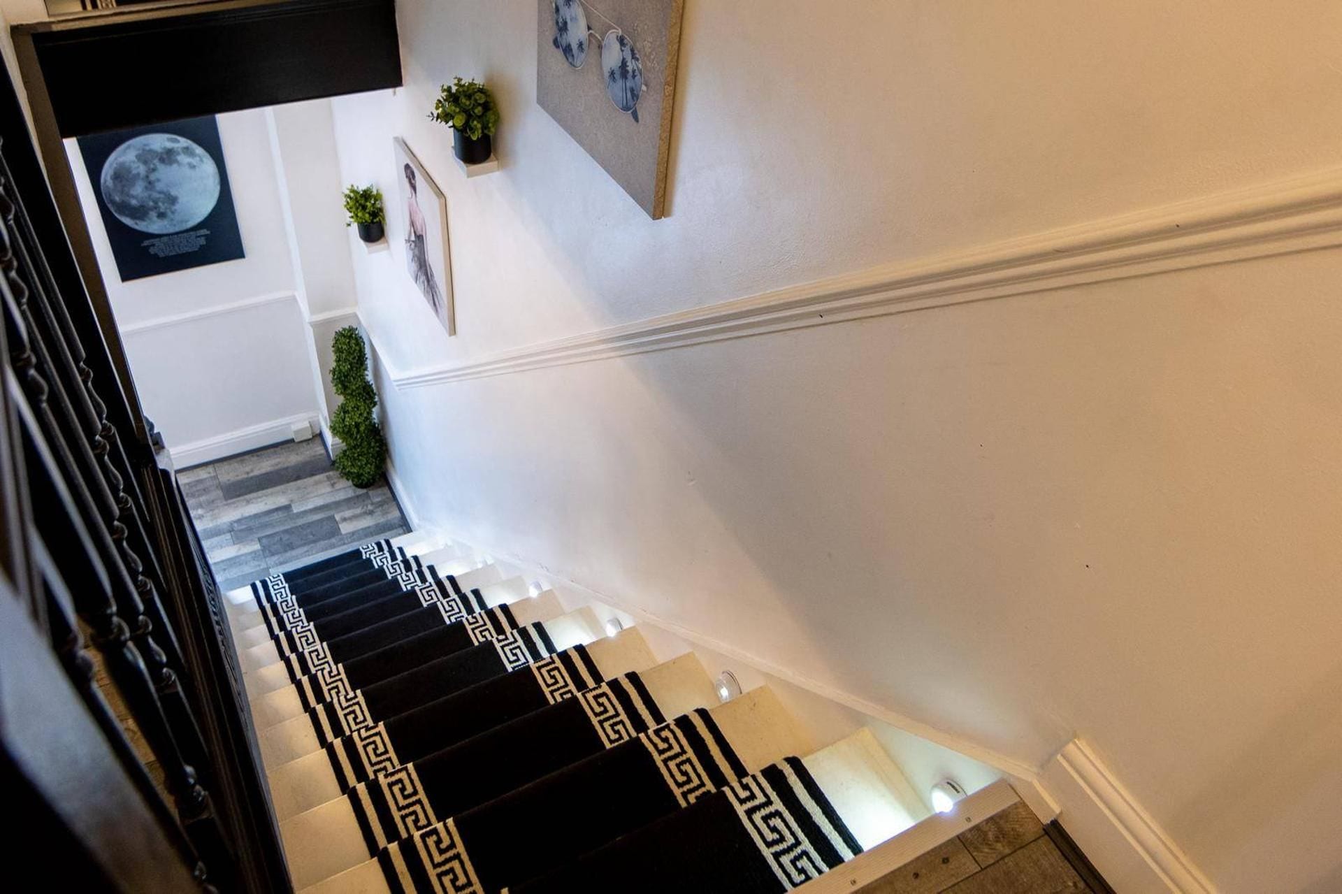Una escalera con un suelo de alfombra a cuadros blanco y negro, paredes blancas y un cuadro con una imagen de la luna.