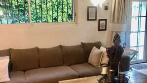 A cozy living room with a large sectional sofa, a wooden coffee table with decorative items, and a view of greenery through a window. - Beautiful ground floor apartment in villa in Opio. (Opio)