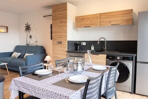 A modern kitchen with a built-in dishwasher, a dining area with a table set for two, and a blue sofa in the living area.