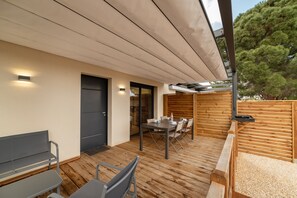 A modern outdoor patio with a wooden deck, a table with chairs, a bench, and a door.