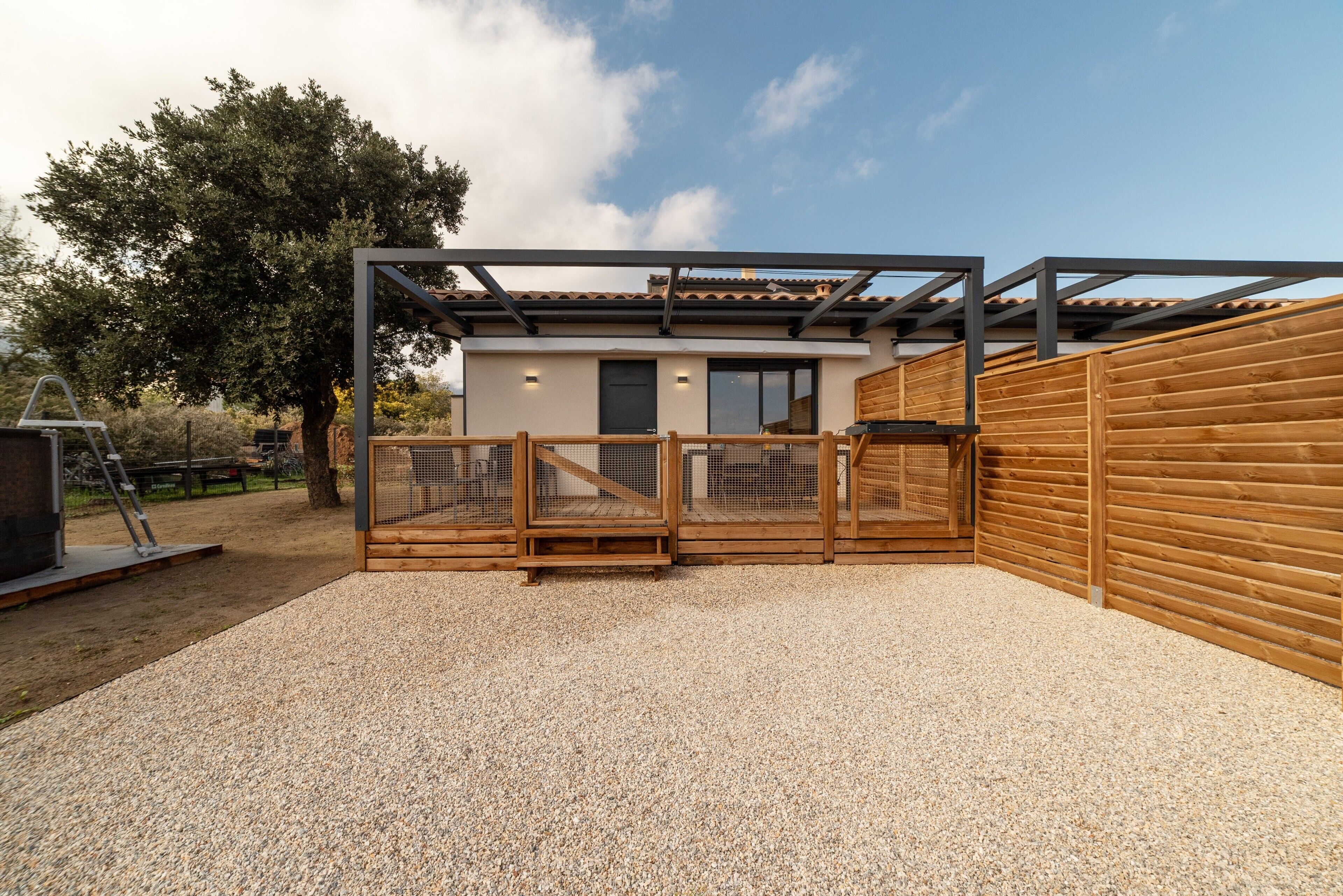 Een modern huis met een houten omheining, een patio van grind en een metalen constructie.