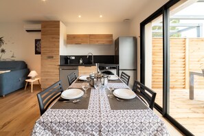 A modern kitchen with wooden cabinets, a dining table set for four, and a large window overlooking a wooden deck. - Charming Gîte 'Côté Mer' with Mountain View, Wi-Fi and Air Conditioning (Sorède)