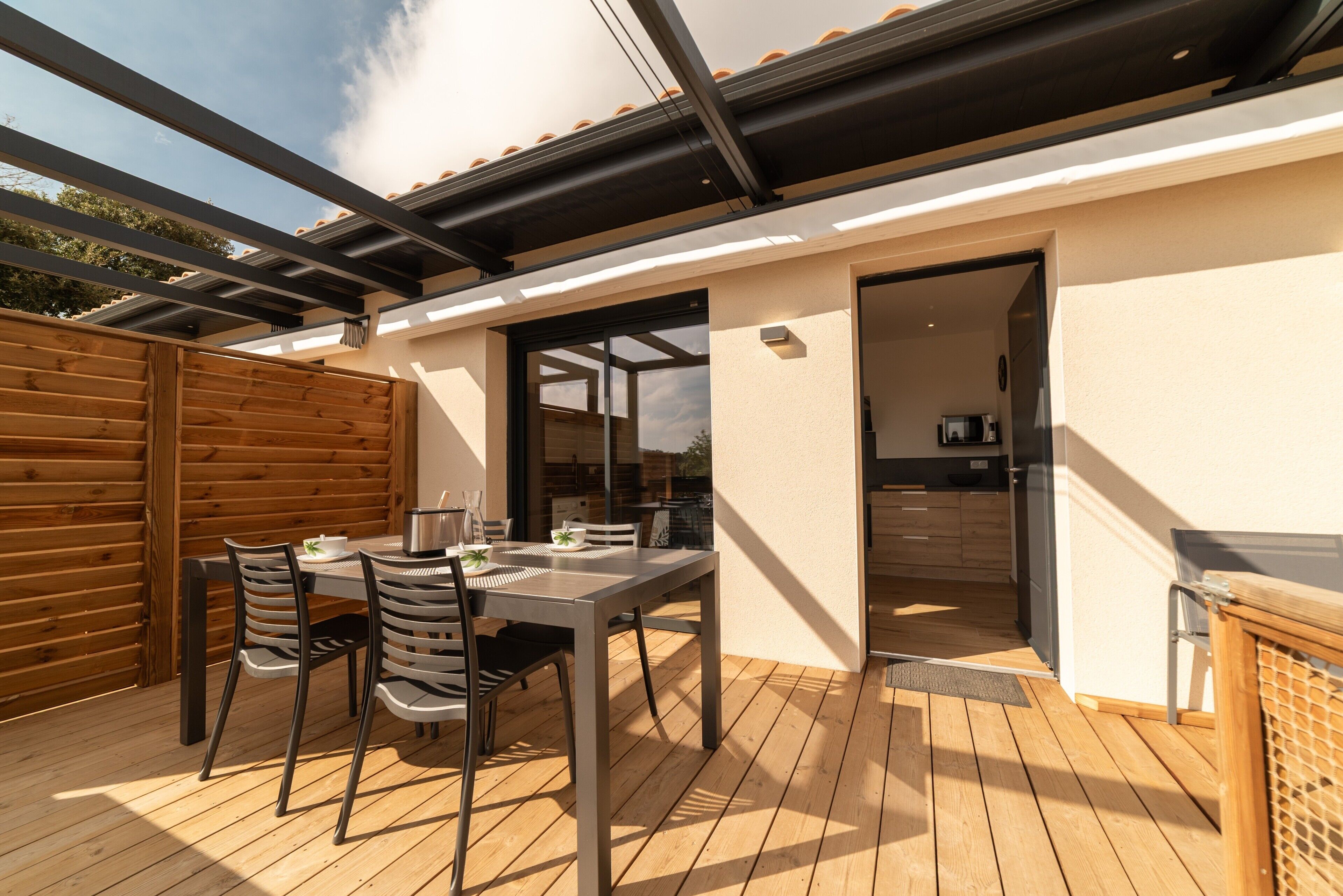 A covered patio with a table and chairs, a wooden fence, and a view of the sky.