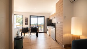 A modern kitchen with a dishwasher, a dining area with a table and chairs, and a view through a glass door to an outdoor deck. - Charming 'Côté Nature' Cottage with Mountain View, Wi-Fi & Air Conditioning (Sorède)