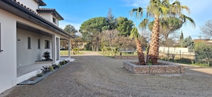 A building with a covered porch, gravel driveway, and palm trees. - Charming 'Côté Nature' Cottage with Mountain View, Wi-Fi & Air Conditioning (Sorède)