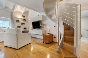 A modern living room with a white sofa, wooden flooring, a TV, and a spiral staircase. - White Residence: central Riva del Garda, private parking and modern design (Riva del Garda)