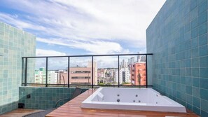 Una terraza en la azotea con un jacuzzi blanco, una cubierta de madera y vistas a la ciudad.