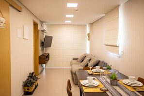 Uma sala de jantar moderna com sofá, mesa posta para dois e televisão na parede.