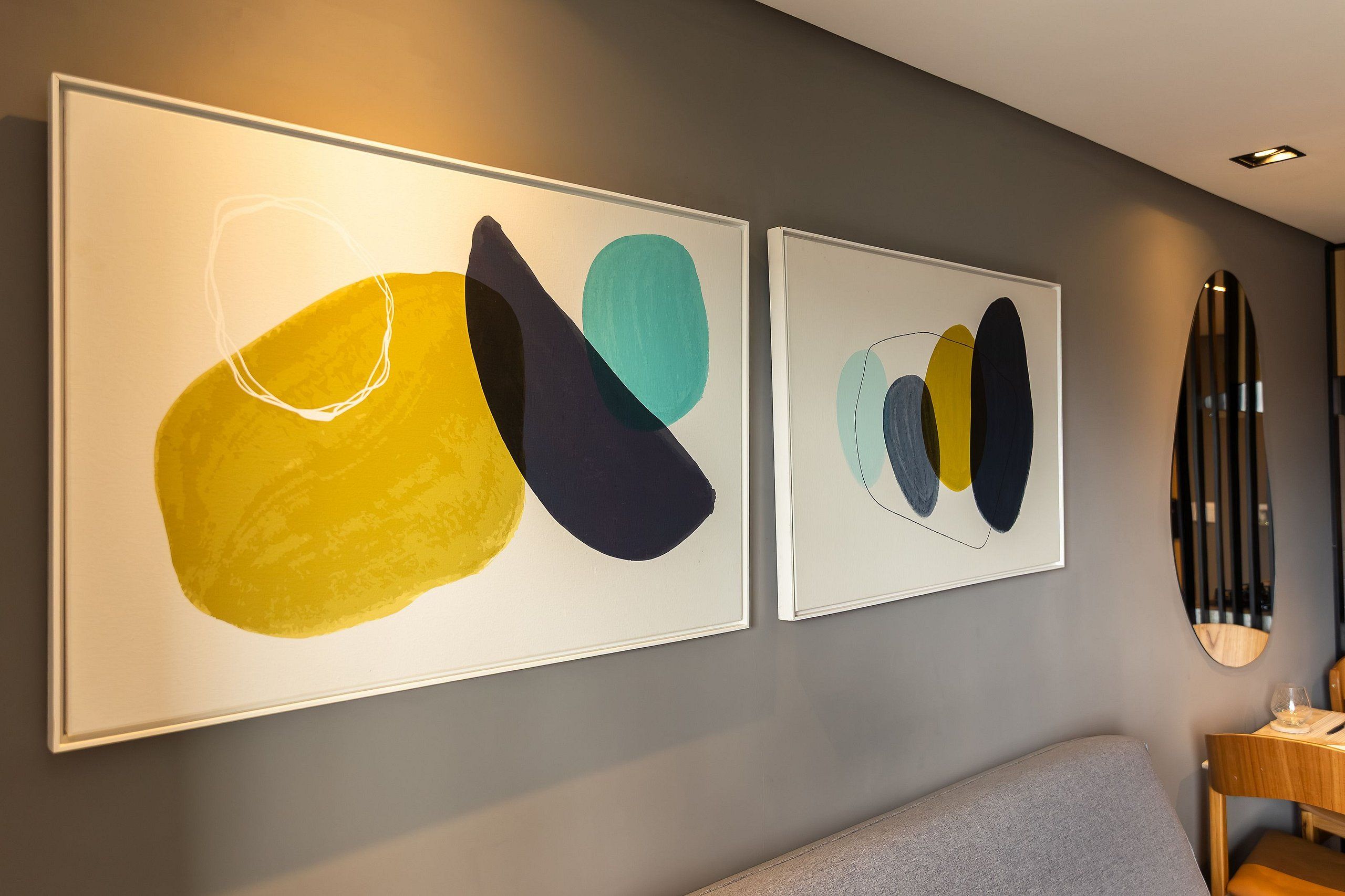 Two abstract paintings on a wall, a gray sofa, and a wooden side table with a glass.