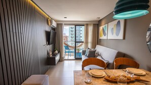 A modern living room with a sofa, dining table set for four, and a view of the outside balcony. - Oceânica Cabo Branco By Carpediem (João Pessoa)
