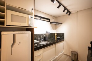 A compact kitchen with a microwave, stove, sink, and overhead lighting.