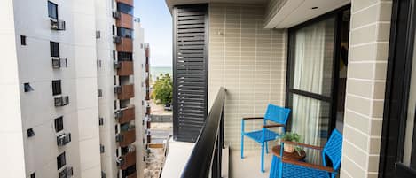 A balcony with blue chairs and a small table, overlooking a pool and adjacent buildings.