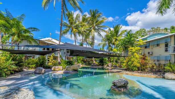 A resort pool with clear water, surrounded by rocks and palm trees. - Wallaby Outlook- Tranquil Trinity Beach Retreat | Pool, Balcony & Nature Views (Trinity Beach)
