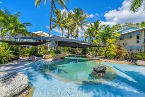 Una piscina de resort con agua cristalina, rodeada de rocas y palmeras.