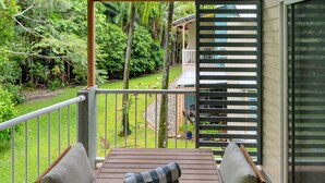 A balcony with a wooden table and two chairs, overlooking a lush garden with various plants and a small pond. - Wallaby Outlook- Tranquil Trinity Beach Retreat | Pool, Balcony & Nature Views (Trinity Beach)