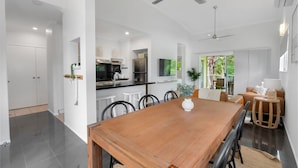 A spacious kitchen with modern appliances, a dining area with a wooden table, and a ceiling fan. - Wallaby Outlook- Tranquil Trinity Beach Retreat | Pool, Balcony & Nature Views (Trinity Beach)