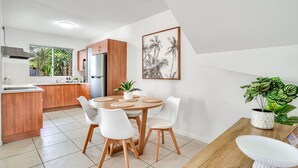 A modern kitchen with wooden cabinets, a stainless steel refrigerator, and a dining area with a round table and white chairs. - Stylish Cairns Escape with Courtyard | Cosmo 14 (Cairns North)
